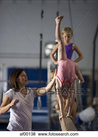 USA, Utah, Orem, Instructor helping gymnasts (6-9) to perform handstand on beam View Large Photo Image Stock Photo - USA, Utah, Orem, Instructor helping gymnasts (6-9) to perform handstand on beam. Fotosearch