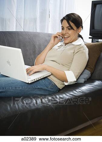 USA, Utah, Orem, woman lying on sofa using laptop and cell phone View Large Photo Image Stock Photo - USA, Utah, Orem, woman lying on sofa using laptop and cell phone. Fotosearch