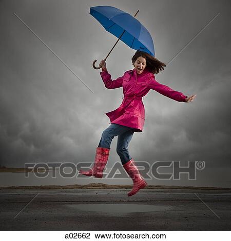 Stock Image - USA, Utah, Orem, woman with umbrella jumping under overcast sky. Fotosearch