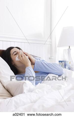 Stock Image - USA, Utah, Orem, young woman sneezing in bed. Fotosearch