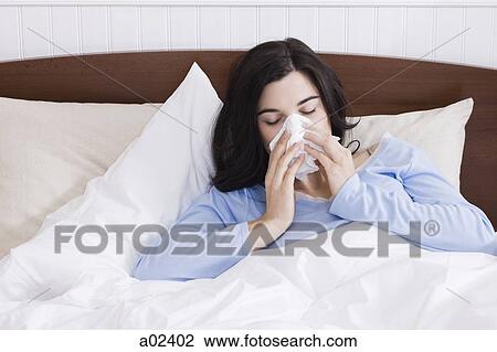 Stock Image - USA, Utah, Orem, young woman sneezing in bed. Fotosearch