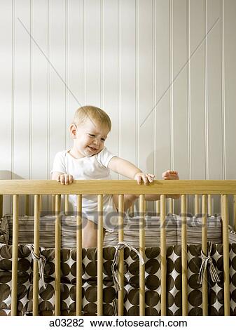 Stock Image - USA, Utah, Provo, Baby boy (18-23 months) climbing in crib. Fotosearch