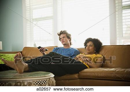 Stock Photo - USA, Utah, Provo, couple sitting on sofa watching TV. Fotosearch