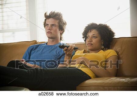 Stock Photo - USA, Utah, Provo, couple sitting on sofa watching TV. Fotosearch