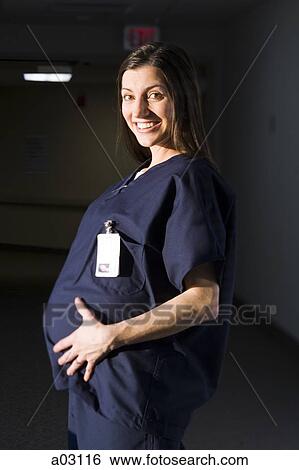 Stock Photograph - USA, Utah, Provo, female pregnant nurse smiling when touching her belly. Fotosearch