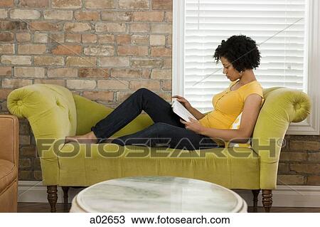 Stock Image - USA, Utah, Provo, woman sitting on sofa and reading book. Fotosearch