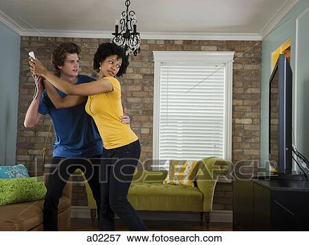 Stock Photo - USA, Utah, Provo, young couple holding remote control in living room. Fotosearch