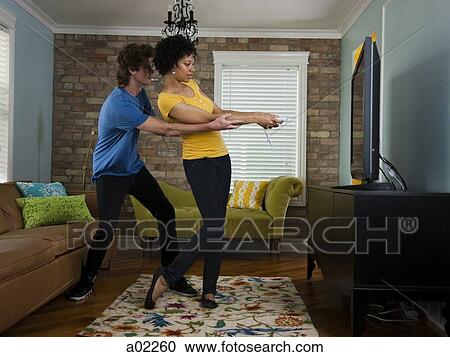 Stock Image - USA, Utah, Provo, young couple using remote control in living room. Fotosearch