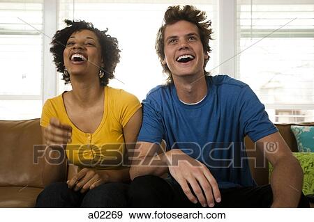 Stock Photo - USA, Utah, Provo, young couple watching television in living room. Fotosearch