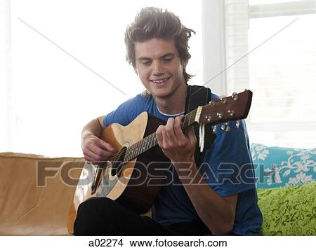 USA, Utah, Provo, young man playing guitar in living room View Large Photo Image Picture - USA, Utah, Provo, young man playing guitar in living room. Fotosearch