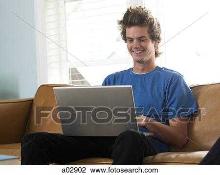 USA, Utah, Provo, young man sitting on sofa and using laptop View Large Photo Image Stock Image - USA, Utah, Provo, young man sitting on sofa and using laptop. Fotosearch