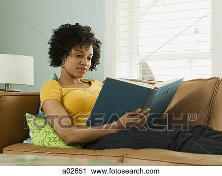 Stock Image - USA, Utah, Provo, young woman lying down on sofa and reading book. Fotosearch