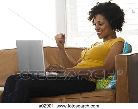 Stock Image - USA, Utah, Provo, young woman sitting on sofa and using laptop. Fotosearch