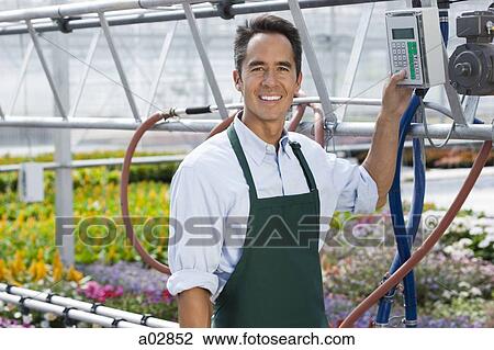 Stock Image - USA, Utah, Salem, portrait of man switching on sprinklers in greenhouse. Fotosearch