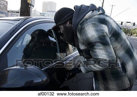 Stock Image - USA, Utah, Salt Lake City, Homeless man peering into car, side view. Fotosearch