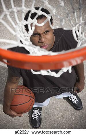 Stock Photo - USA, Utah, Salt Lake City, young man looking up at basketball hoop. Fotosearch