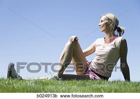 Stock Image - woman sitting on the grass stretching. Fotosearch