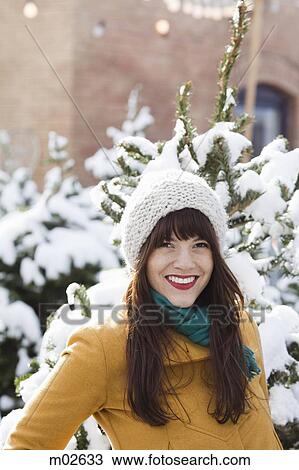 Stock Image - woman standing in the snow in a grove of fir trees. Fotosearch