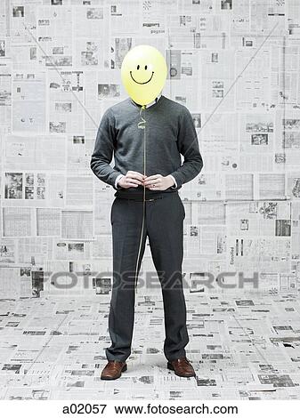 Young man covering face with smiley balloon in newspaper room View Large Photo Image Stock Photo - Young man covering face with smiley balloon in newspaper room. Fotosearch