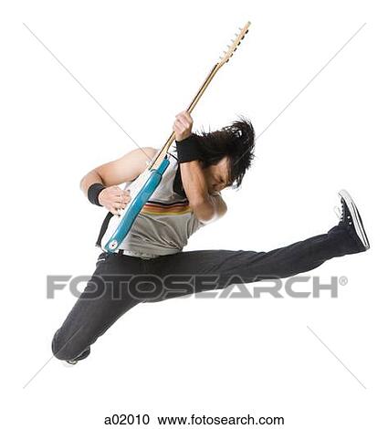 Stock Image - Young man jumping and playing guitar, studio shot. Fotosearch