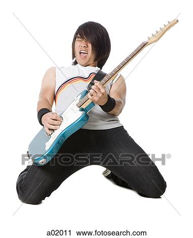 Stock Image - Young man kneeling and playing electric guitar, studio shot. Fotosearch