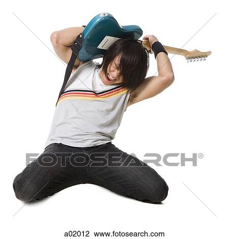 Stock Image - Young man kneeling and playing electric guitar, studio shot. Fotosearch