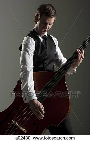 Young man playing double bass like a guitar, studio shot View Large Photo Image Stock Image - Young man playing double bass like a guitar, studio shot. Fotosearch