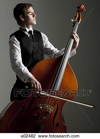 Young man playing double bass, studio shot View Large Photo Image Stock Image - Young man playing double bass, studio shot. Fotosearch