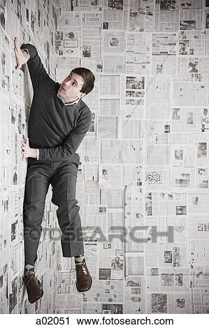 Stock Image - Young man stuck to wall covered with newspapers trying to escape, studio shot. Fotosearch