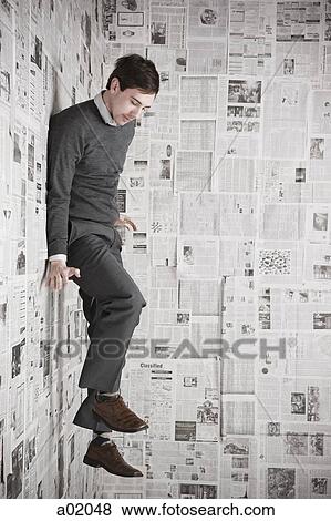 Stock Photo - Young man stuck to wall covered with newspapers, studio shot. Fotosearch