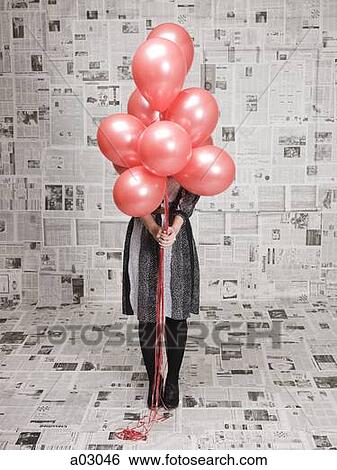 Young woman hiding face behind bunch of balloons in newspapers covered room, studio shot View Large Photo Image Stock Photograph - Young woman hiding face behind bunch of balloons in newspapers covered room, studio shot. Fotosearch