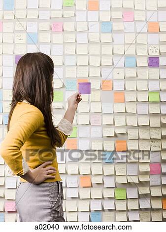 Young woman holding piece of paper in front of wall covered with adhesive notes View Large Photo Image Stock Image - Young woman holding piece of paper in front of wall covered with adhesive notes. Fotosearch