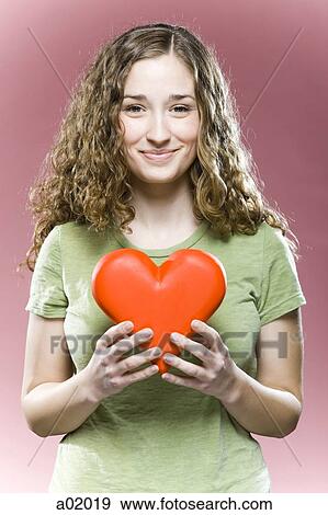 Stock Photo - Young woman holding red heart, portrait. Fotosearch