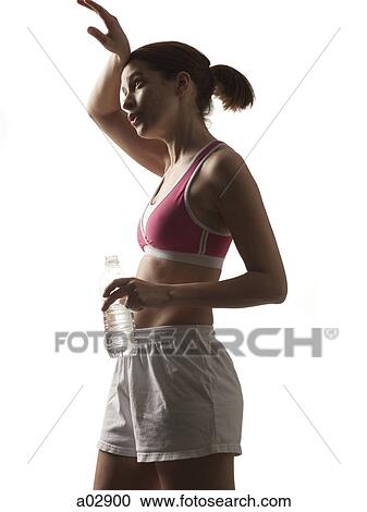 Stock Image - Young woman in sportswear drinking water, studio shot. Fotosearch