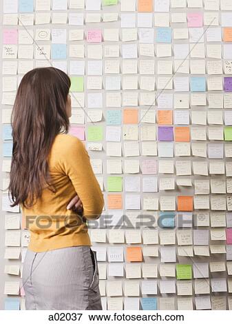 Stock Photo - Young woman looking at wall covered with adhesive notes. Fotosearch