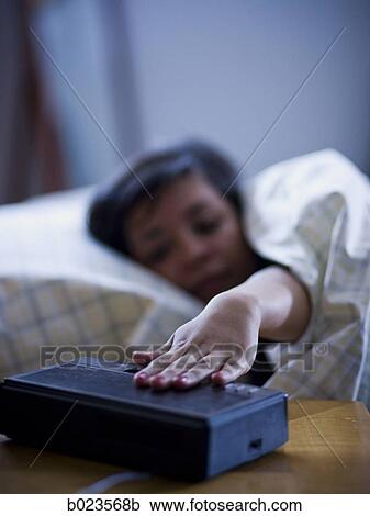 Stock Image - young woman reaching for alarm clock. Fotosearch
