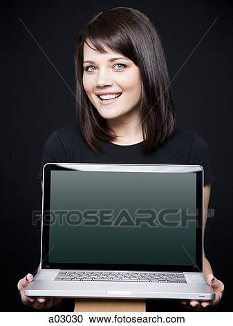 Stock Image - Young woman showing laptop, studio shot. Fotosearch