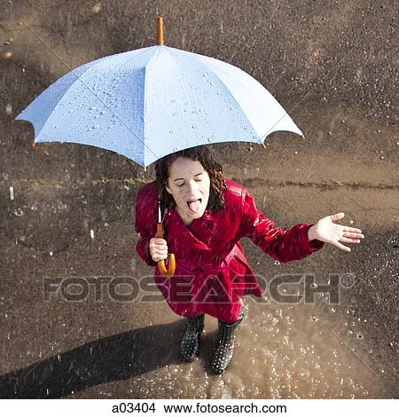Young woman standing in rain holding umbrella View Large Photo Image Picture - Young woman standing in rain holding umbrella. Fotosearch