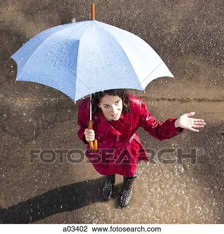 Stock Image - Young woman standing in rain holding umbrella. Fotosearch