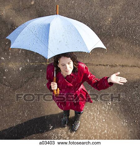 Stock Image - Young woman standing in rain holding umbrella. Fotosearch