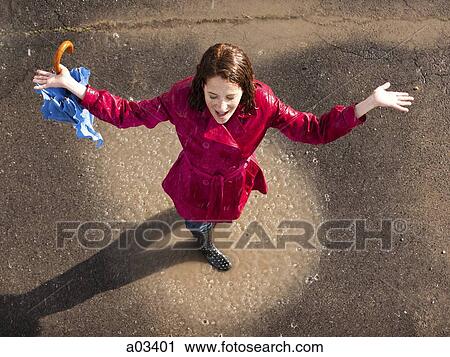 Stock Image - Young woman standing in rain with arms outstretched. Fotosearch