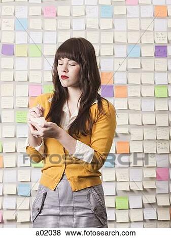 Stock Photo - Young woman writing in front of wall covered with adhesive notes. Fotosearch