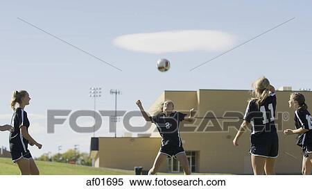 Athlete with soccer teammates hitting ball with head in soccer goal under blue sky View Large Photo Image Stock Photography - Athlete with soccer teammates hitting ball with head in soccer goal under blue sky. Fotosearch