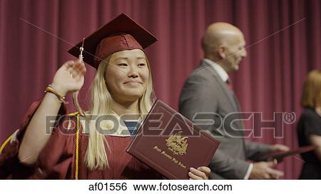 Stock Photograph - Blurred view of waving student holding diploma on stage during graduation ceremony. Fotosearch