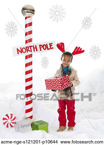 Boy (4-5) wearing reindeer antlers standing next to North Pole sign View Large Photo Image Picture - Boy (4-5) wearing reindeer antlers standing next to North Pole sign. Fotosearch