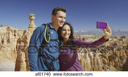 Boyfriend and girlfriend taking selfie with smartphone near scenic rock formations in remote landscape under clear blue sky View Large Photo Image Stock Image - Boyfriend and girlfriend taking selfie with smartphone near scenic rock formations in remote landscape under clear blue sky. Fotosearch