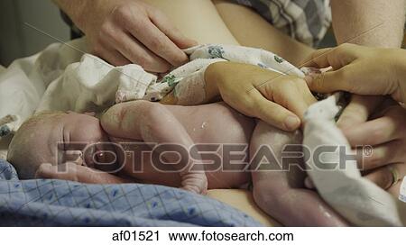 Stock Image - Close up of parents' hands cleaning newborn baby in hospital. Fotosearch