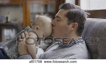 Close up profile of father kissing baby daughter's hair on sofa View Large Photo Image Stock Photo - Close up profile of father kissing baby daughter's hair on sofa. Fotosearch