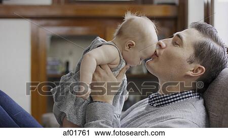 Close up profile of smiling father kissing baby daughter's forehead on sofa View Large Photo Image Stock Image - Close up profile of smiling father kissing baby daughter's forehead on sofa. Fotosearch