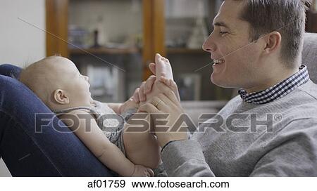 Close up profile of smiling father playing with baby daughter's feet on sofa View Large Photo Image Stock Photo - Close up profile of smiling father playing with baby daughter's feet on sofa. Fotosearch